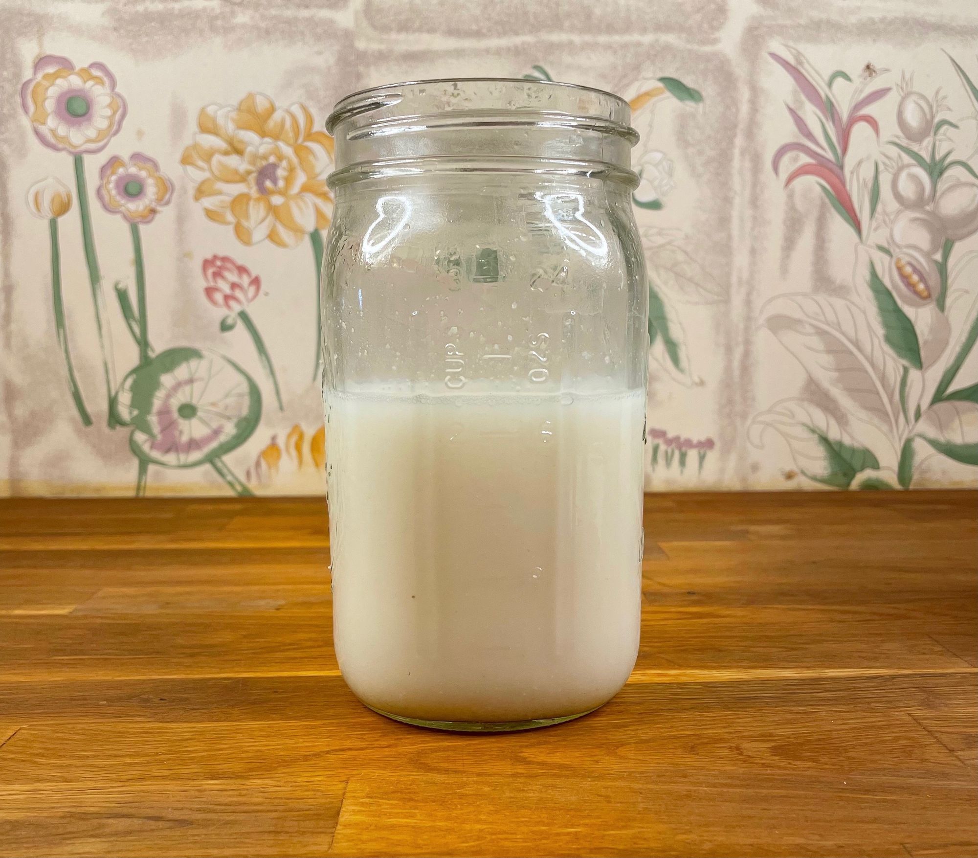 An open mason jar of milk on a wooden countertop. 