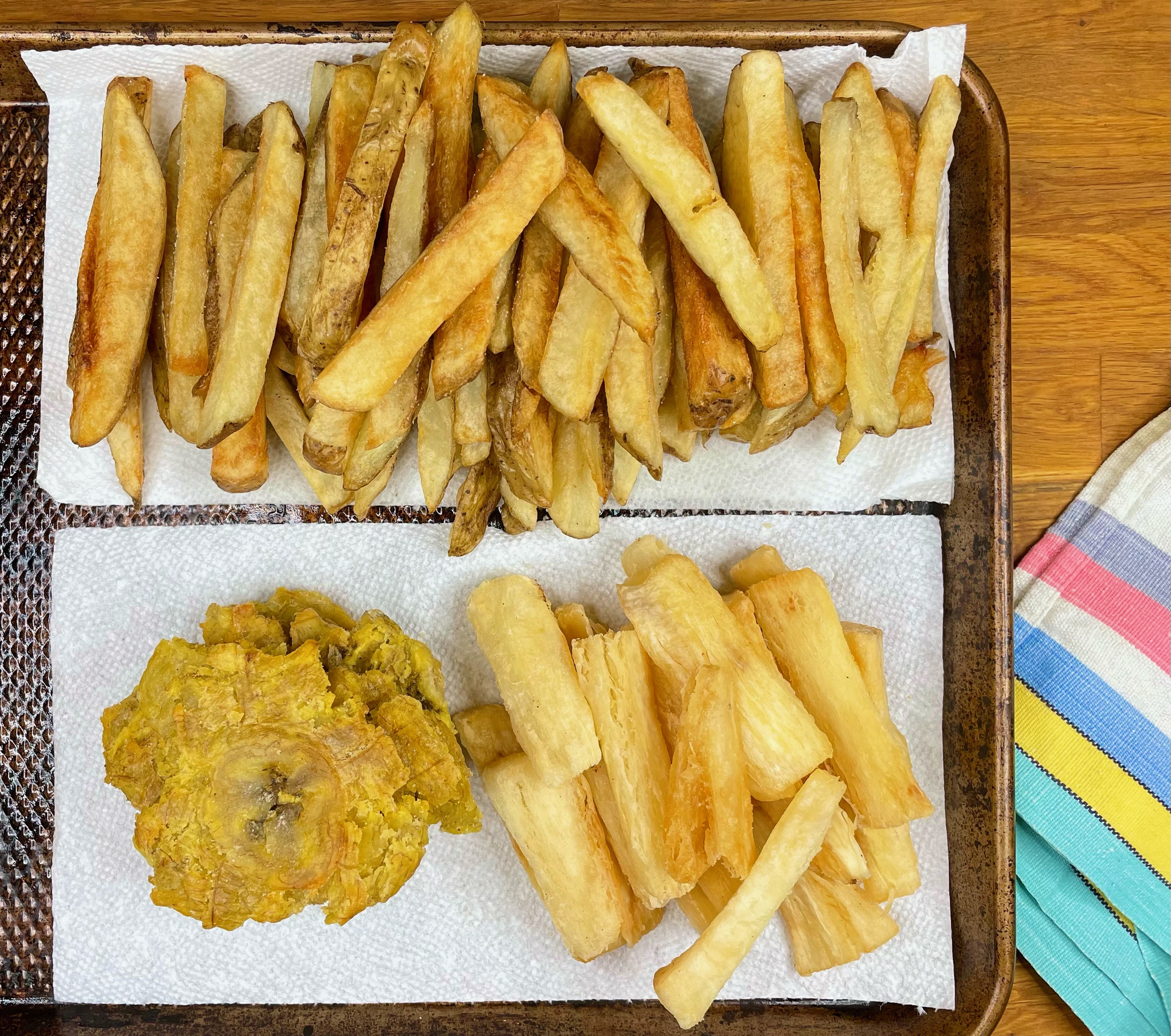 Fried potatoes, yuca root, and plantains on a cookie sheet. 
